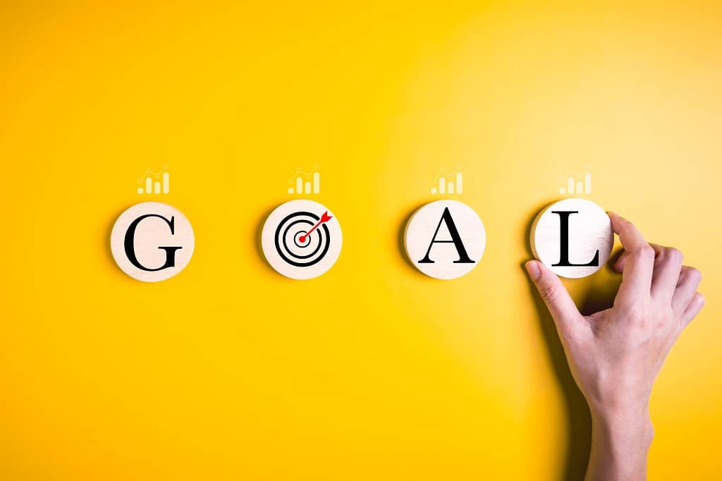 Article campagne social ads - Vue sur une main tenant un rond en bois "L" à côté d'autres ronds formant ensemble le mot "GOAL" sur un fond jaune
