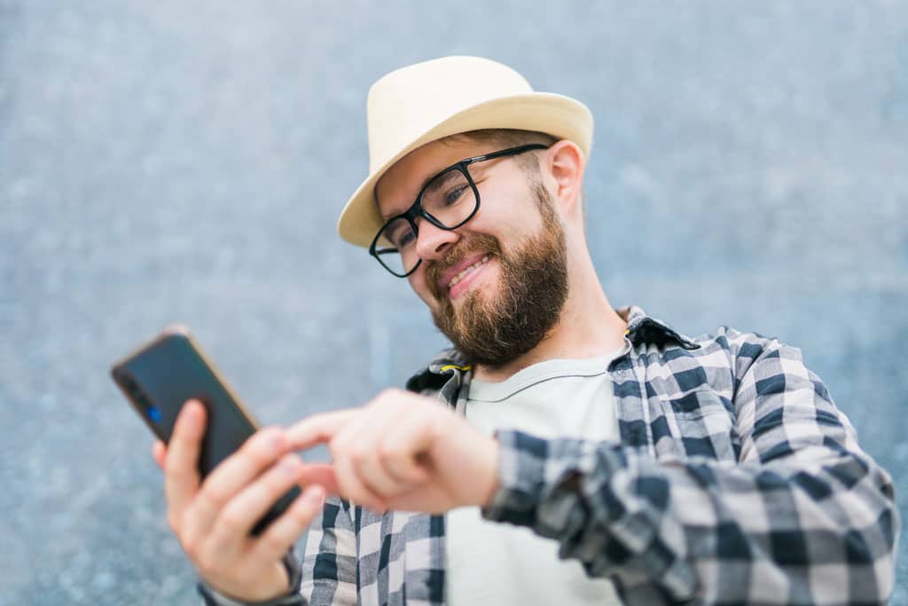 Article carrousel sur facebook - Un homme souriant qui navigue sur son smartphone.
