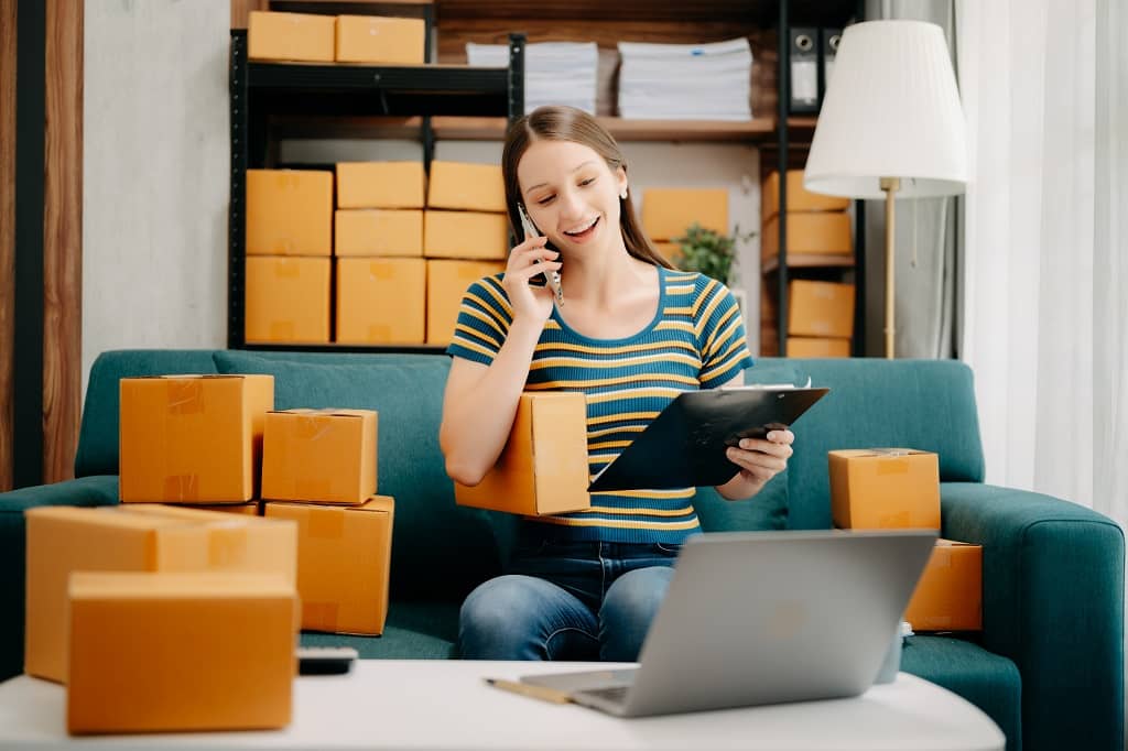 Article exemple publication facebook - Une femme assise discutant au téléphone, vérifiant une liste en main et qui est entourée de boîtes