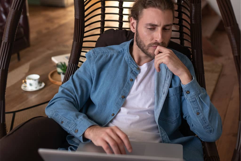 Article idées noms instagram - Un homme pensif assis dans une chaise avec son ordinateur sur ses jambes