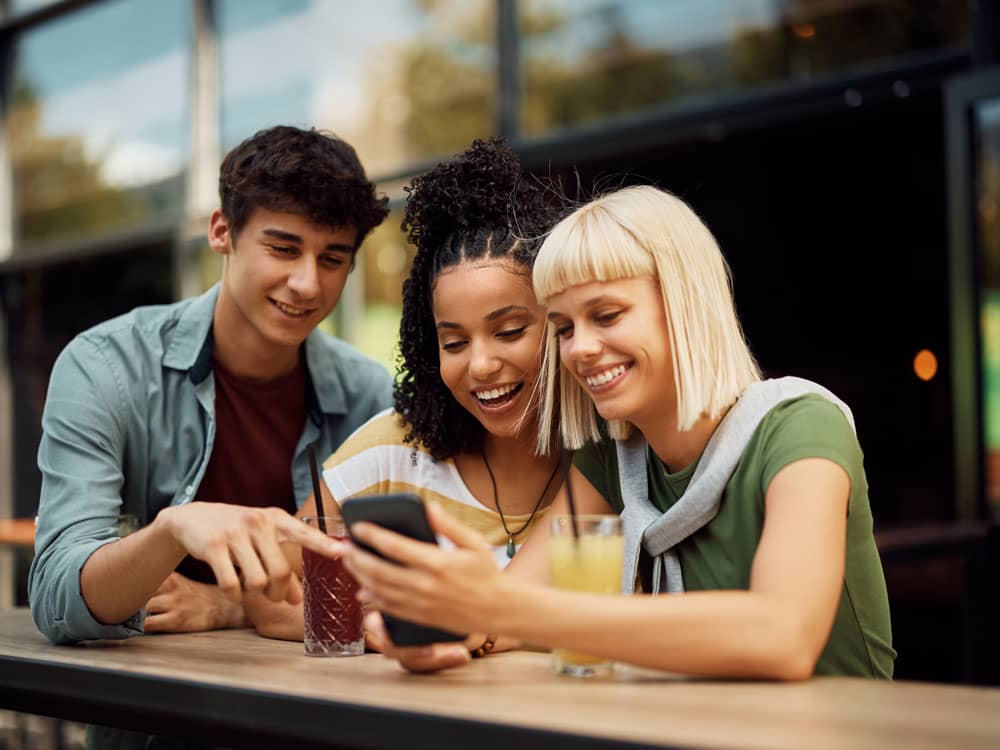 Article instagram followers - Trois personnes rigolant dans un bar et regardant un téléphone