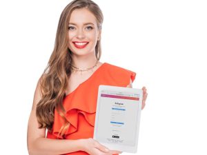 Article instagram pour les nuls - Une femme souriante regardant la caméra en montrant une tablette affichant la page de connexion d'Instagram