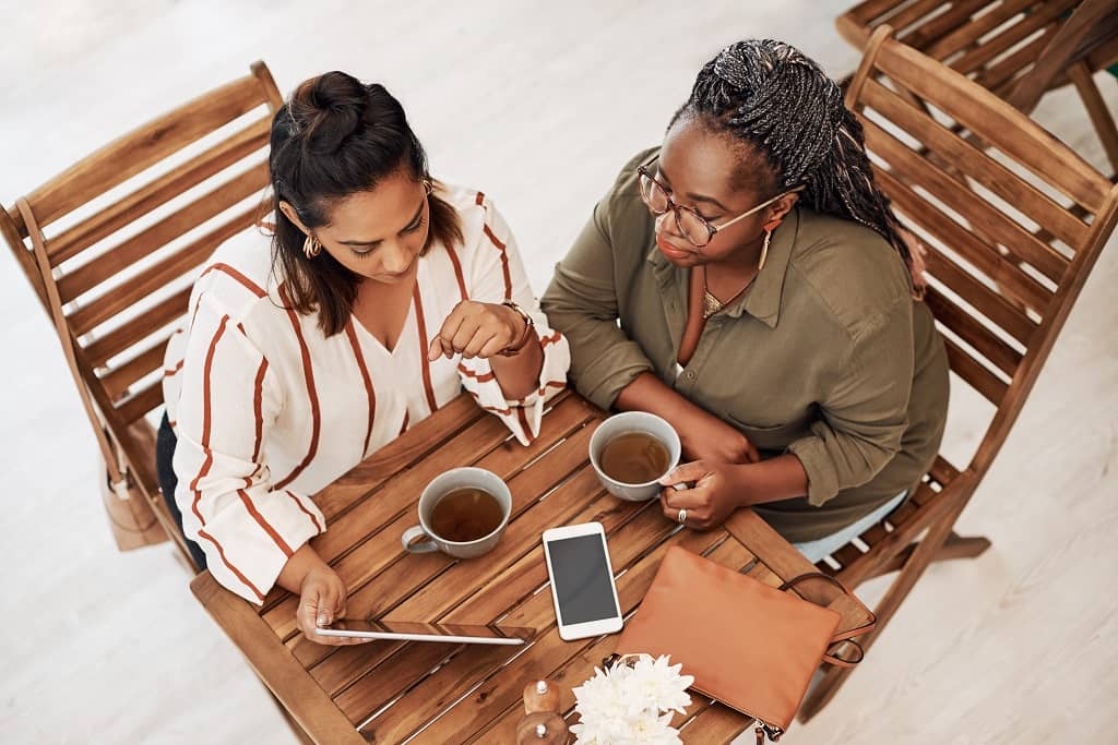 Article instagram pour les nuls - Vue en plongée sur deux femmes buvant une boisson en terrasse et regardant une tablette