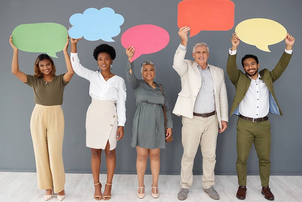 Article instagram pour les nuls - Cinq personnes debout regardant la caméra en souriant et en tenant en hauteur des affiches en forme de bulles de dialogue