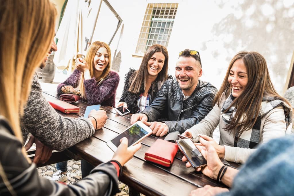 Article instagram pour les nuls - Un groupe d'amis assis autour d'une table rigolant et regardant leur téléphone