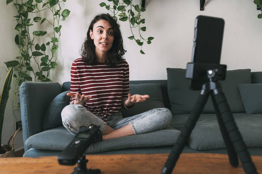 Article social ads définition - Une femme assise sur son canapé en tailleur se filmant en train de parler