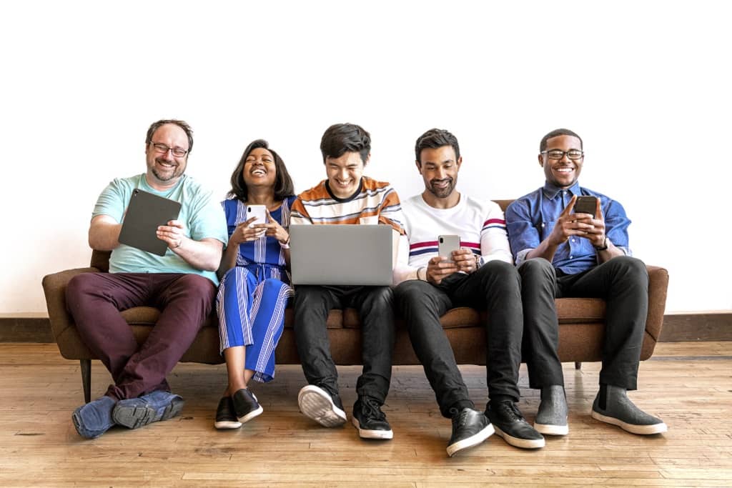Article social ads définition - Un groupe de personnes assises sur un canapé rigolant devant leur tablette, téléphone et ordinateur