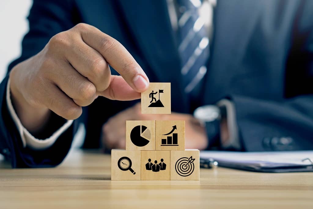 Article social ads définition - Vue sur la main d'un homme posant un cube en bois sur d'autres illustrant des objectifs