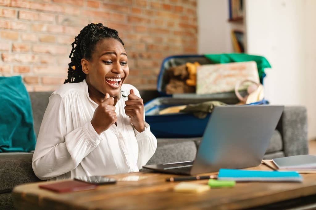 Article tirage au sort concours instagram - Une femme assise par terre à sa table basse heureuse devant son ordinateur 